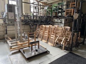 Wood chair in stress test eqiupment along with other wood chairs stacked beside.
