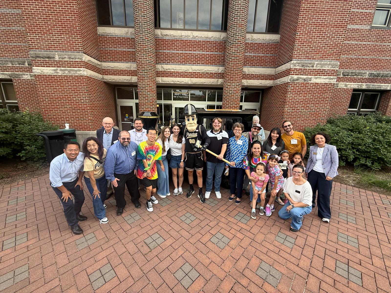 Group of people standing with Purdue Pete in front of a brick building