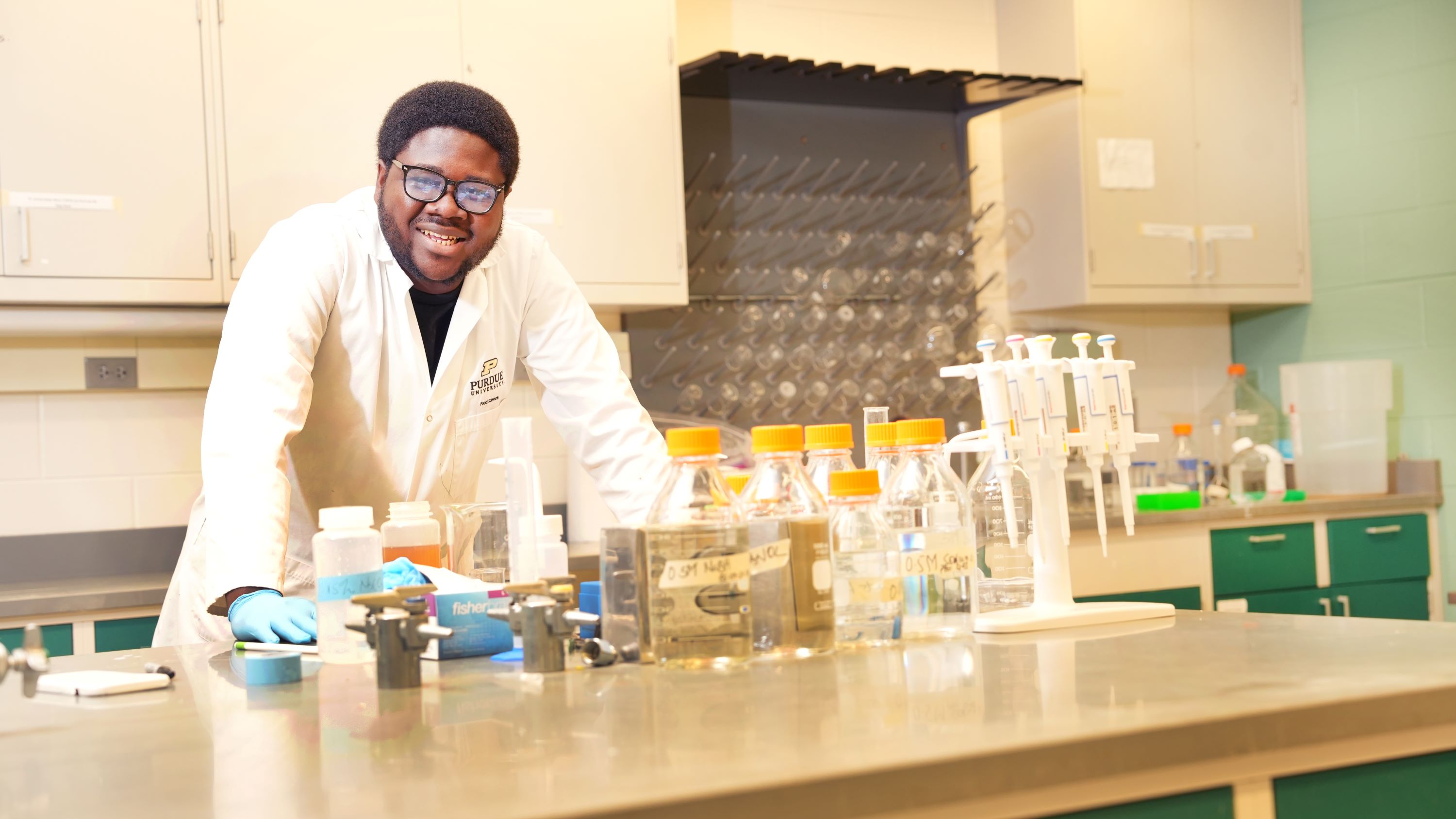 Student standing in a lab behind lab equipment and supplies