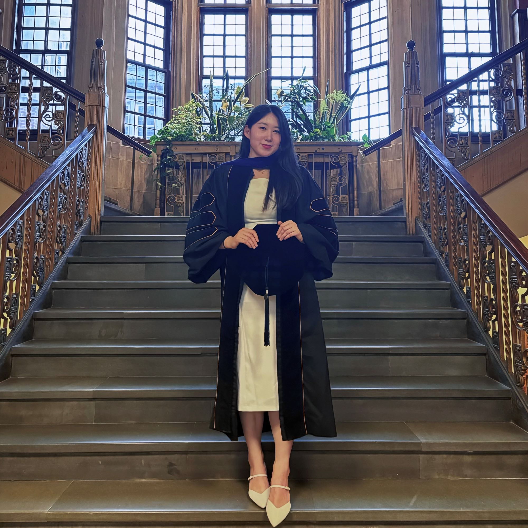 Woman standing on a staircase while holding a graduation cap