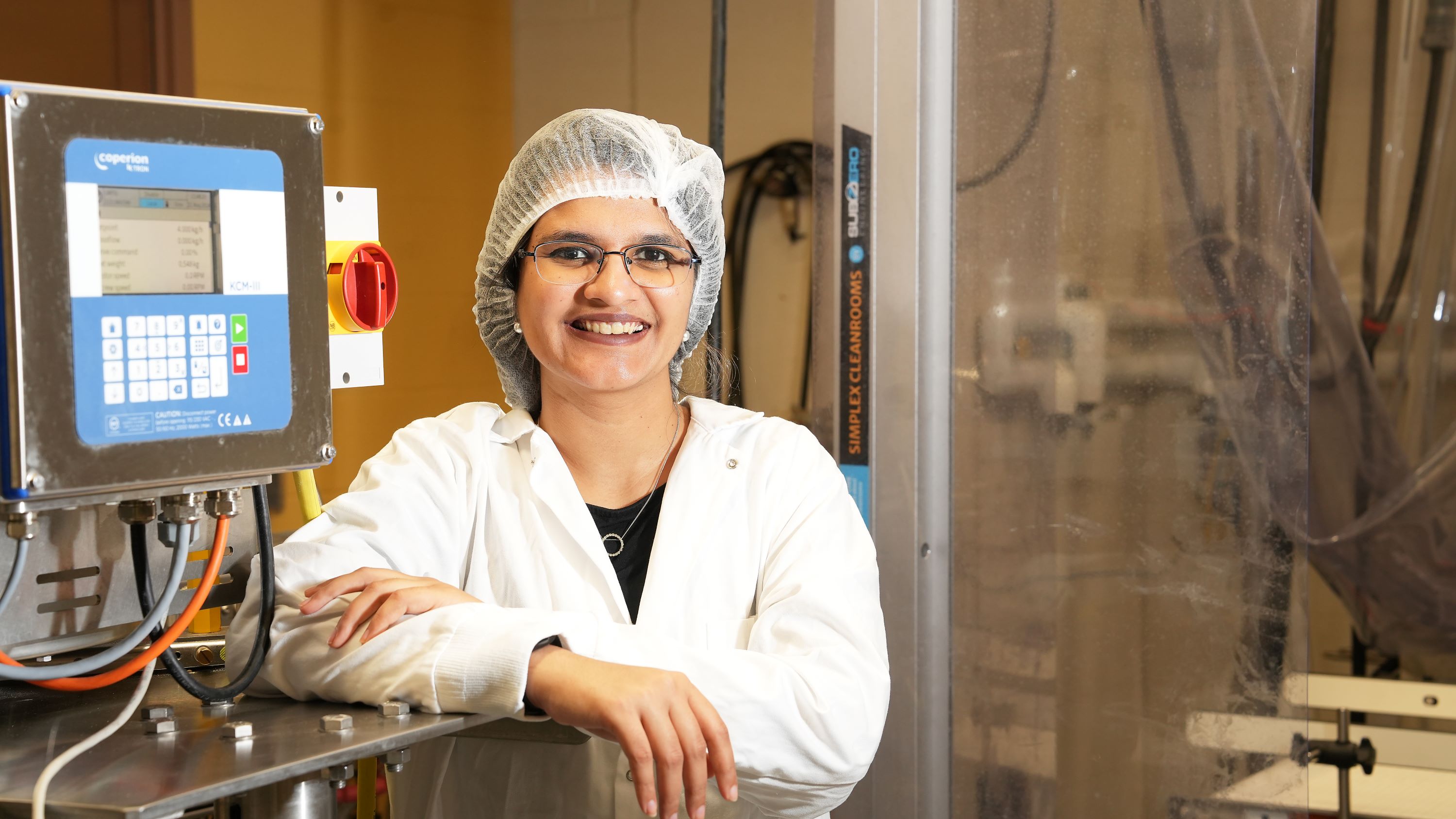 Student in a hair net standing next to an equipment panel