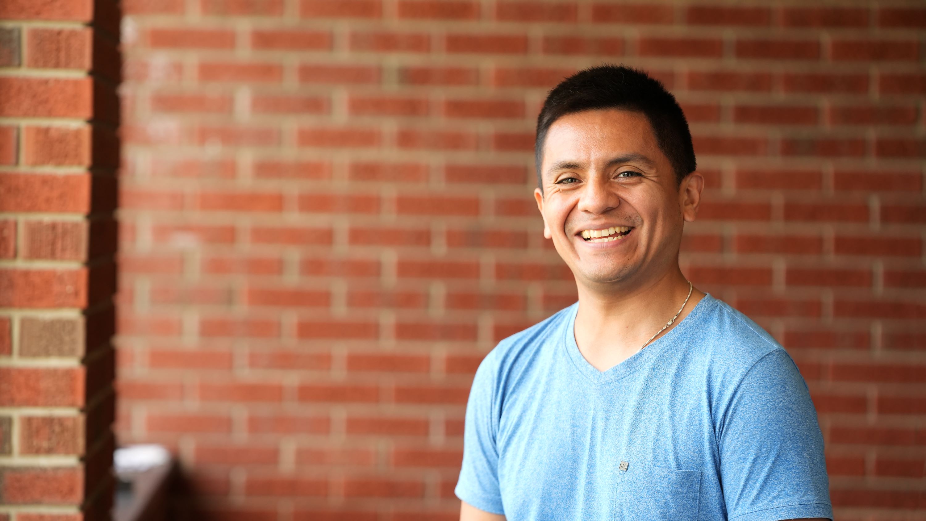 Student smiling while standing in front of red brick wall