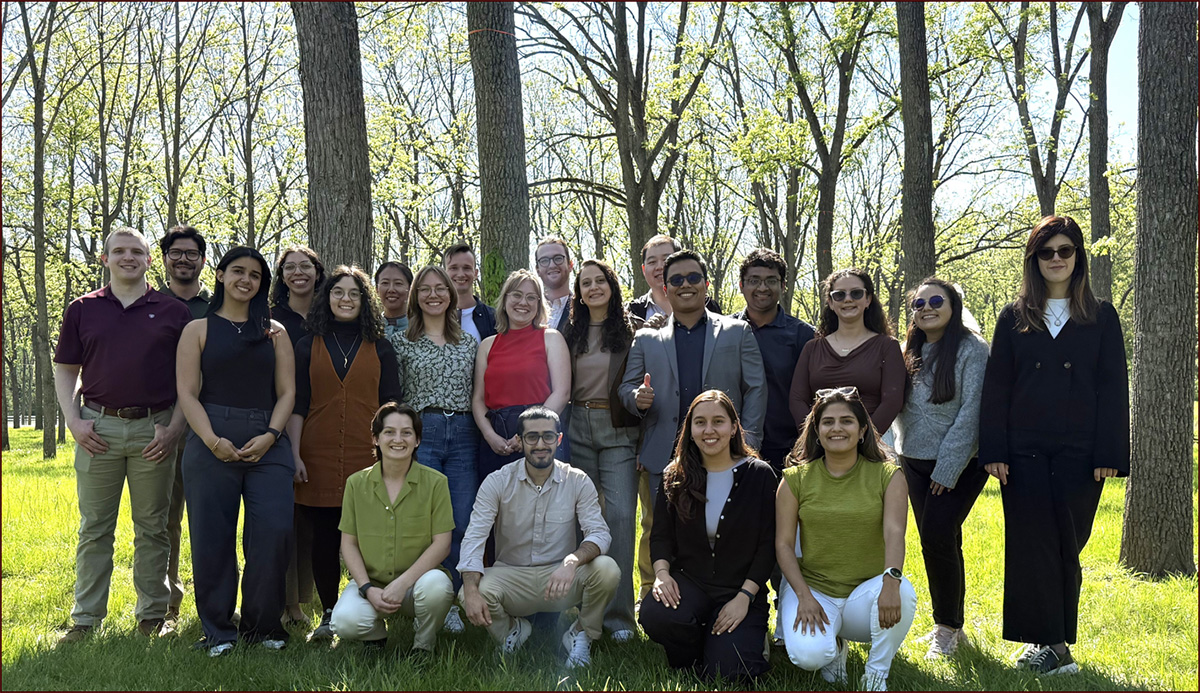 Graduate students pose for a group photo outdoors among trees during a departmental retreat.