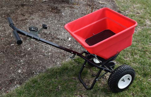 Rotary spreader positioned beside a landscape bed for applying granular fertilizer.