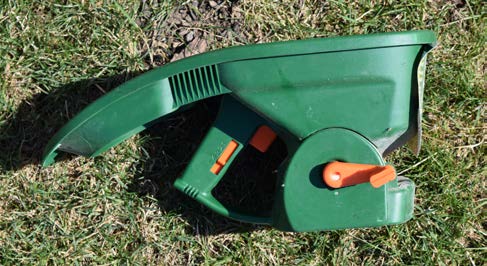 Hand-held fertilizer spreader resting on turf grass.
