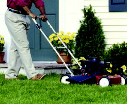 Person pushing a lawn mower across a residential yard near a house