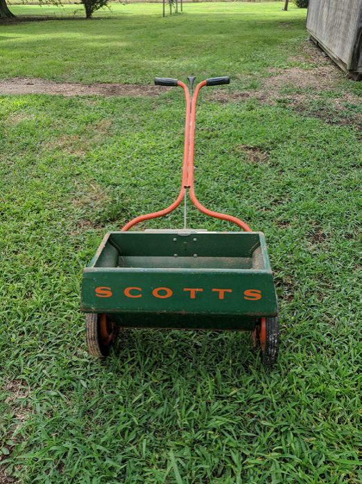 A green drop spreader with its front facing the camera. "SCOTTS" in orange is printed across the front.