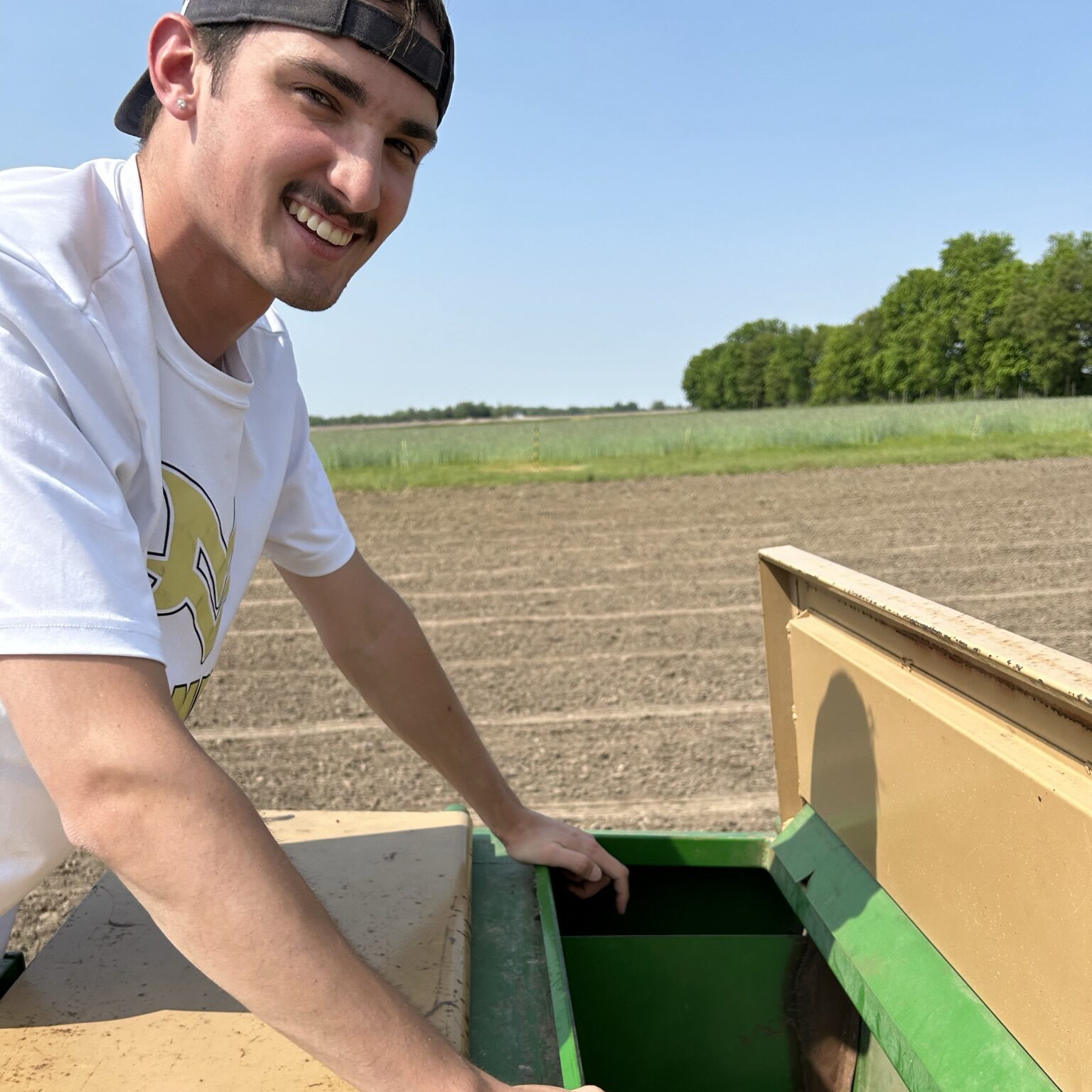 Student researcher operating agricultural field equipment at a research farm.