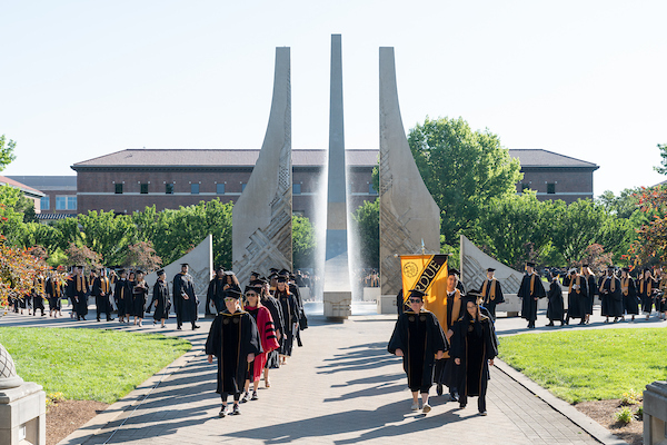 Agriculture students in graduation caps and gowns walk in two lines in front of the Engineering fountain