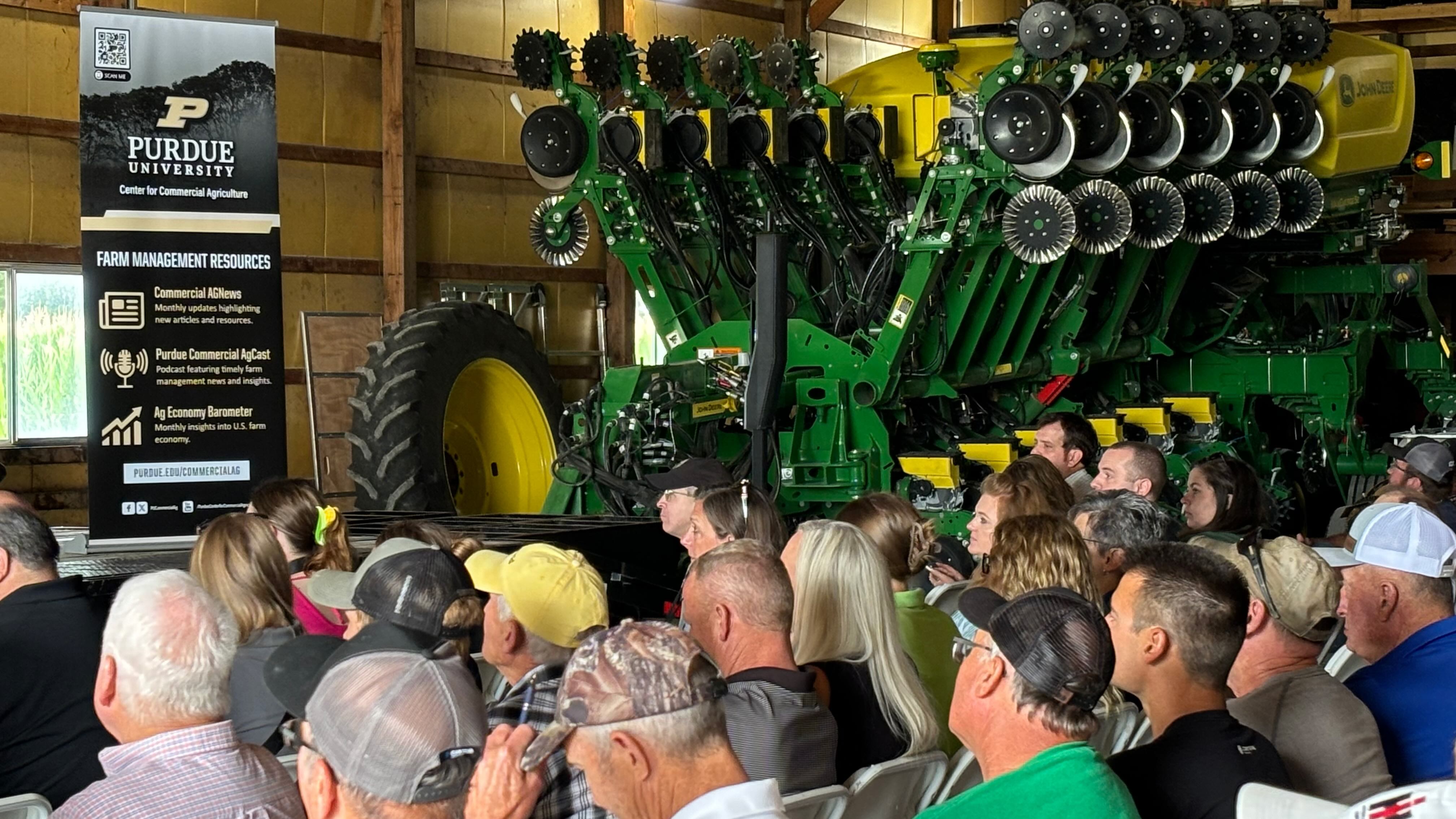 audience seated in a barn at the 2024 Purdue Farm Management Tour event next to a large green John Deere planter