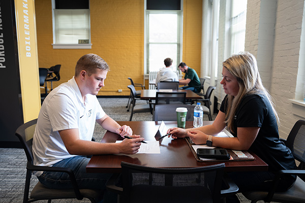 A student sits at a table with an employer as they look over their paper resume