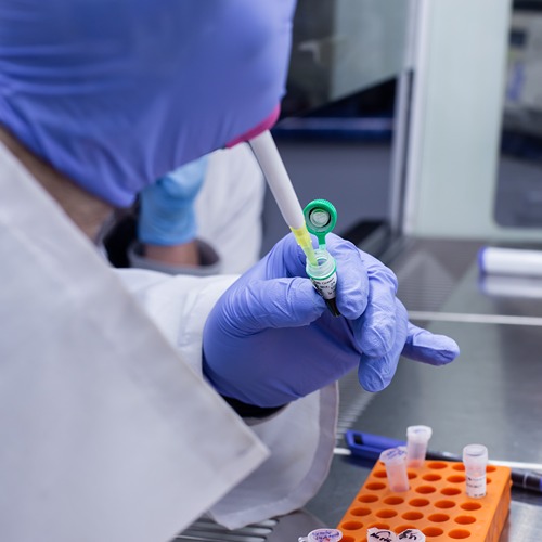 purple gloved hand uses a micropipette to take up green liquid from a small test tube