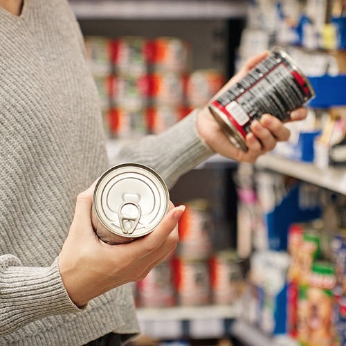 a person in a gray sweater holds a can in each hand in the grocery store, comparing the labels