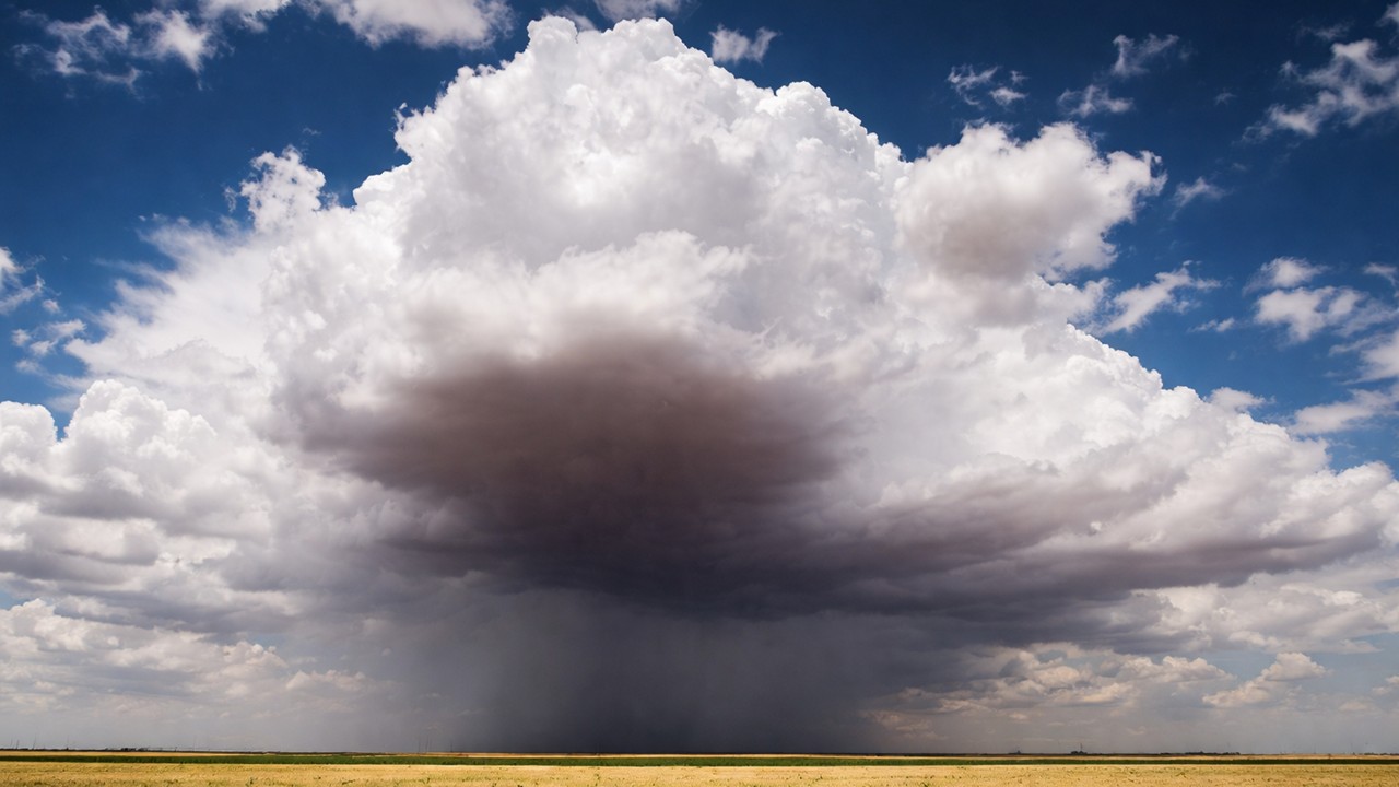 Large thunderstorm cloud producing rain over flat Midwestern farmland