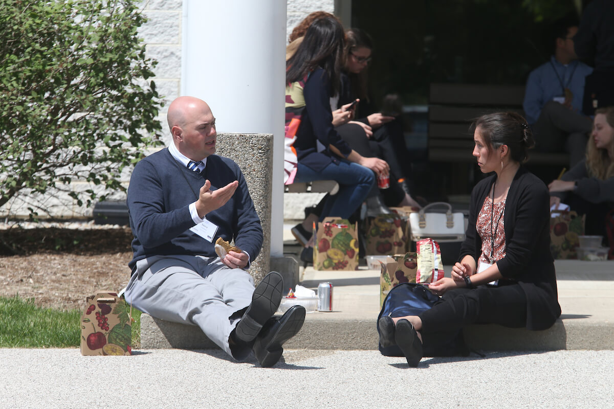 Two adult seated in the sidewalk talking while eating their meal