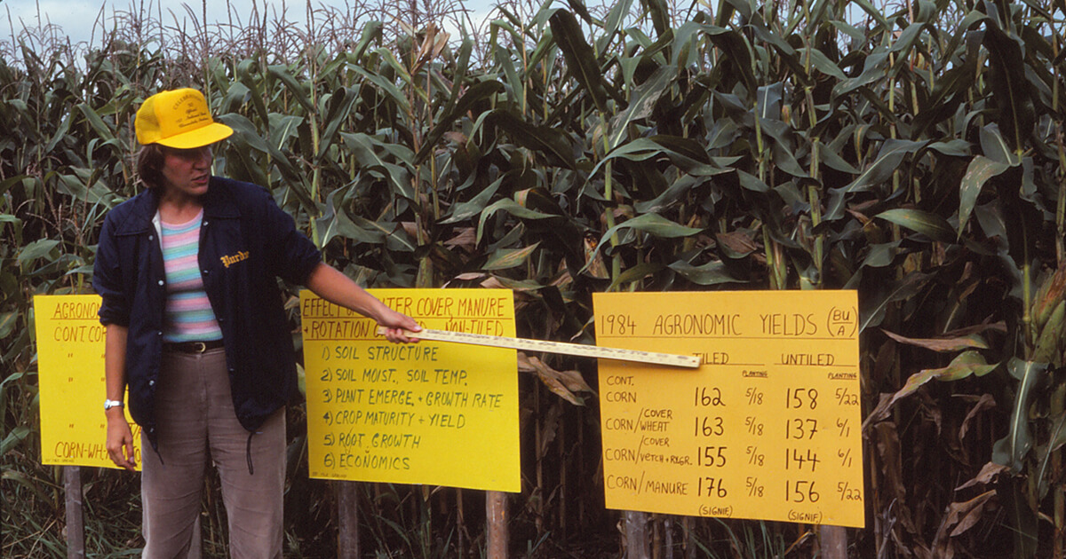 Eileen Kladivko outdoors in a cornfield explaining a chart banner