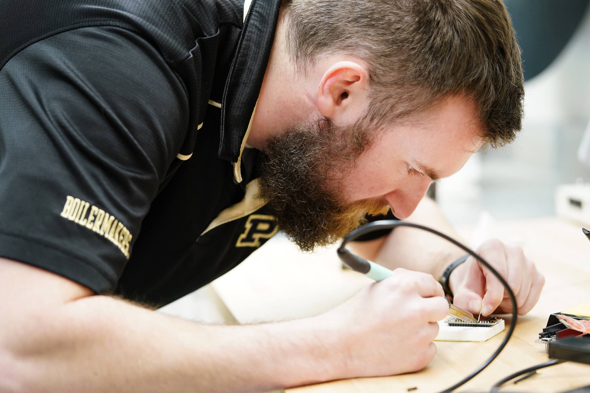  Male student solders a small circuit board.