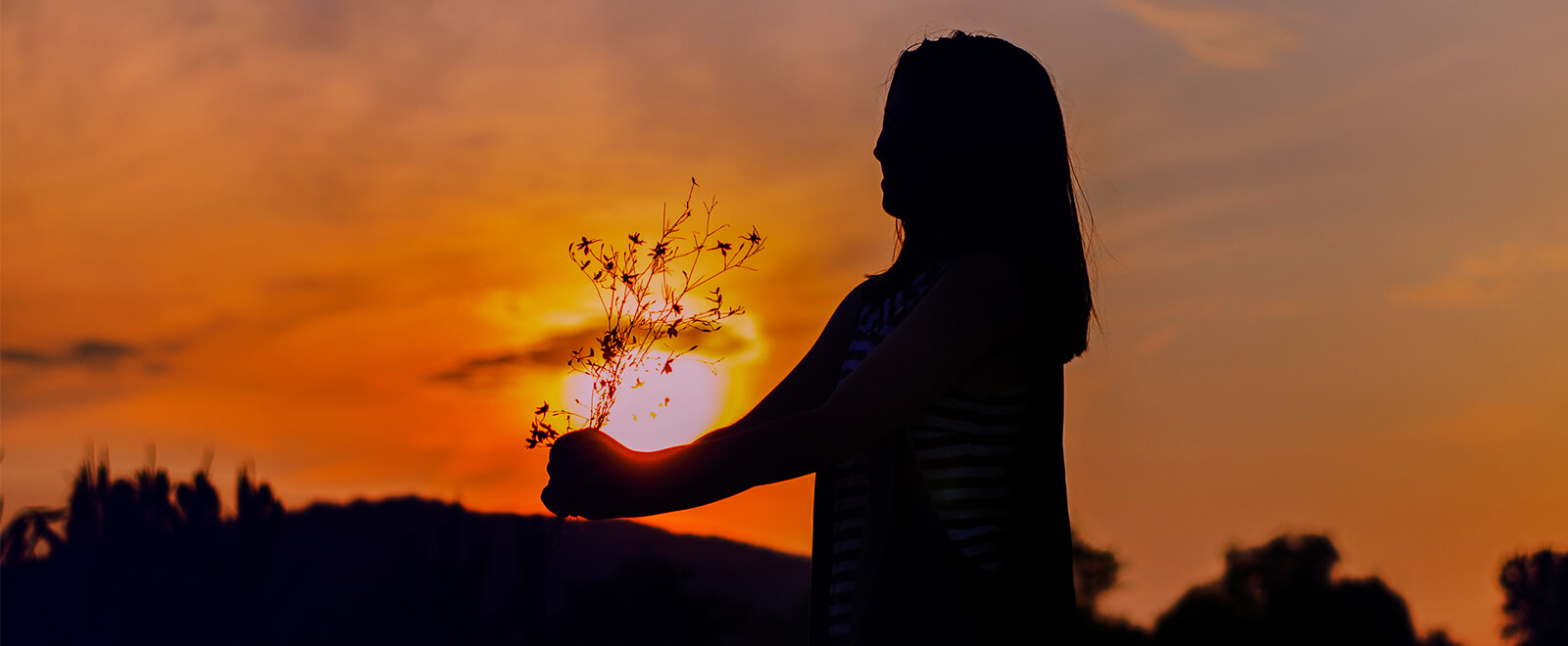 Young lady holding a bunch of flowers with the yellow sunset in the background