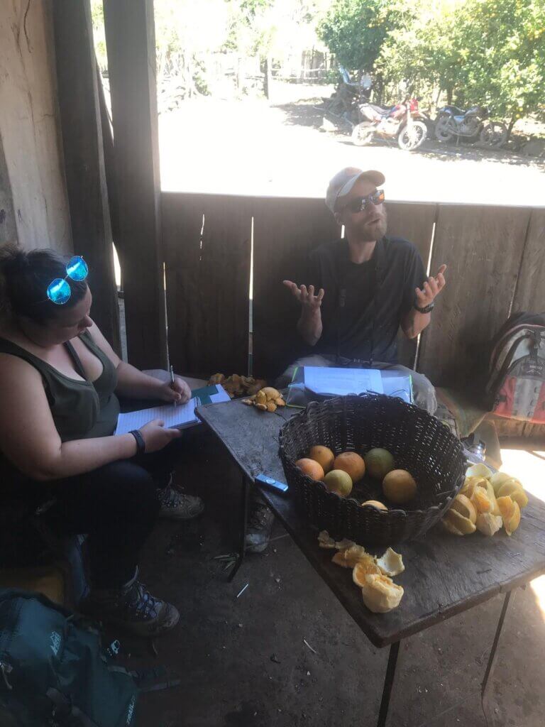 BROOKE MCWHERTER inside a small cabin writing her research with locals in the mountains of Bolivia (basket of oranges in the table) 