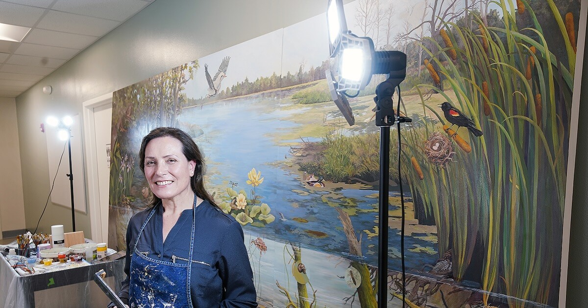 Artist Gabriela Sincich smiling, her mural painting in the background
