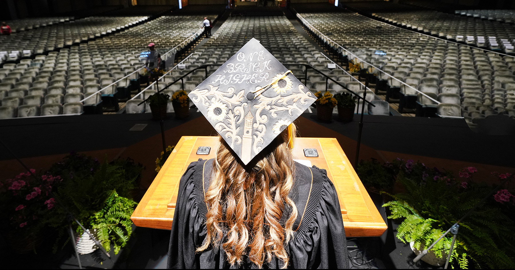 Grace Hasler standing at podium wearing a graduation cap and facing an empty hall