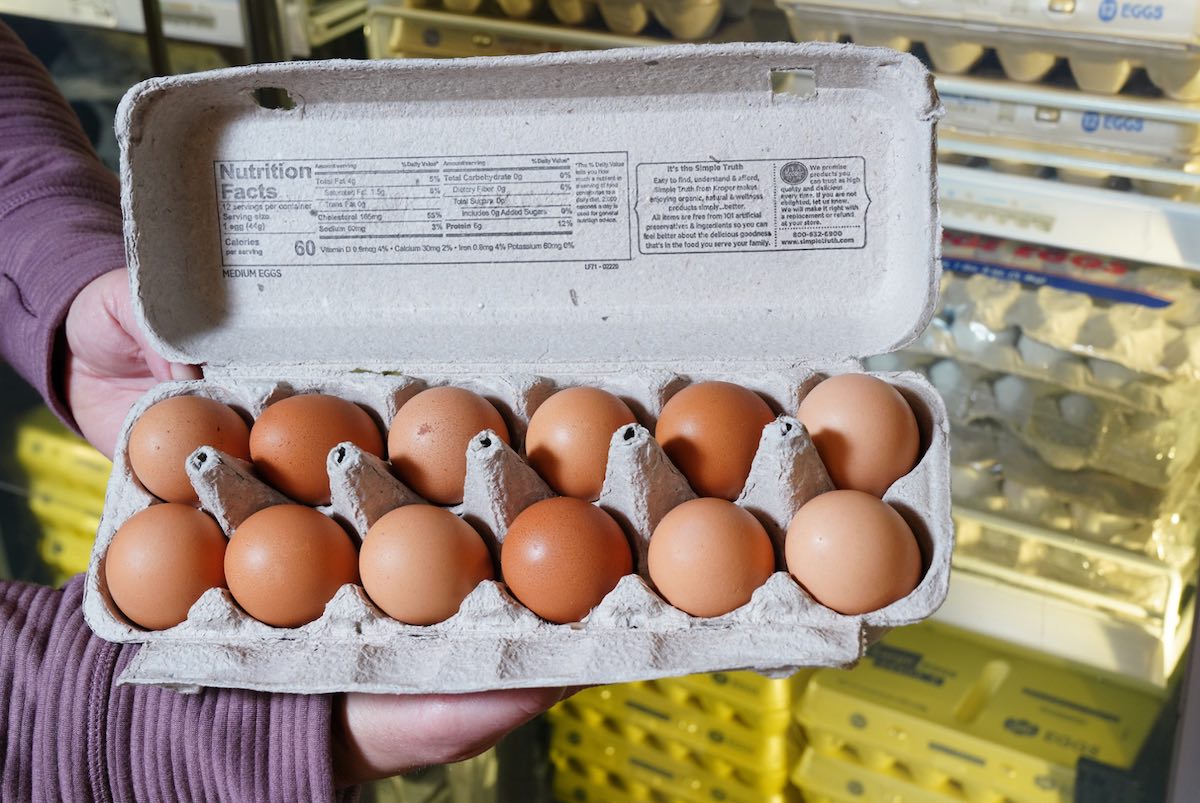 A dozen brown eggs sit in an open carton.