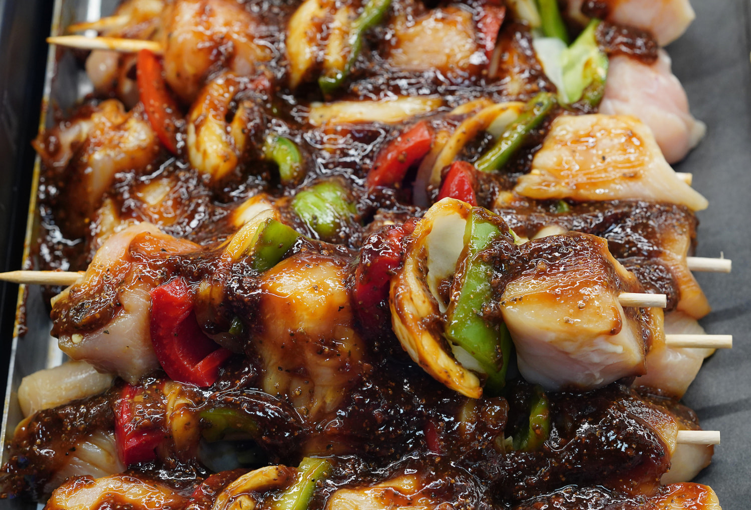 Skewers of chicken and vegetables cook atop a grill.