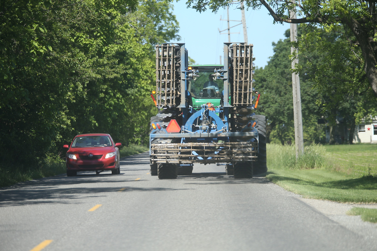 farm implement driving down a narrow road 