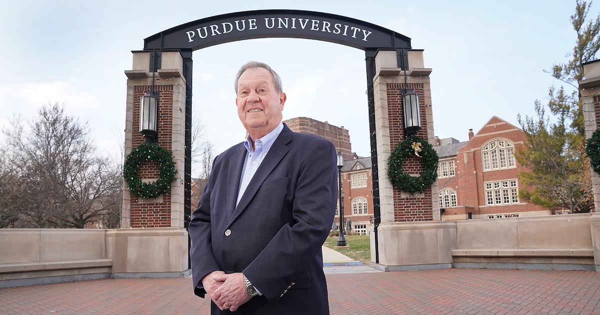John Baugh stands beneath the Purdue University State and Grant Street Gateway.