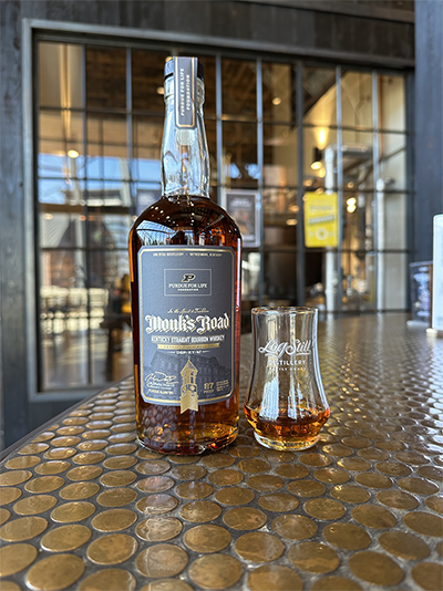 Monk's Road Bourbon bottle and glass of bourbon next to it.