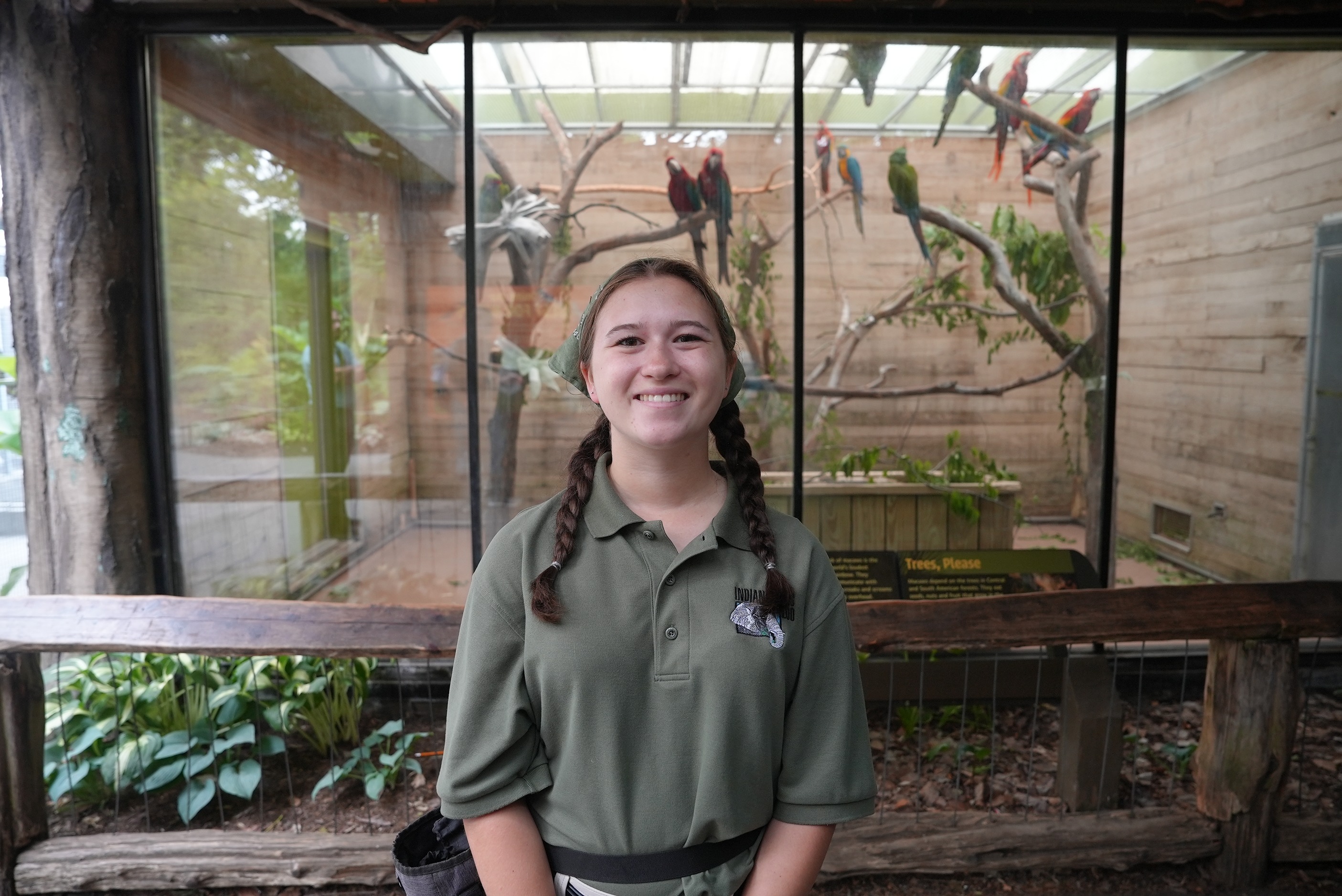 Emily Carlisle stands in front of the macaw enclosure with one of the zoo's three flocks behind her