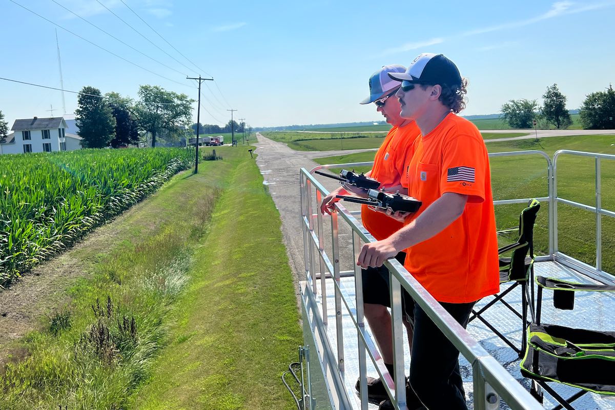Ryan Lieberman (left) and Alex Hokey (right) stand on a trailer and monitor their drones spraying Illinois farmer Rich Birkey's field
