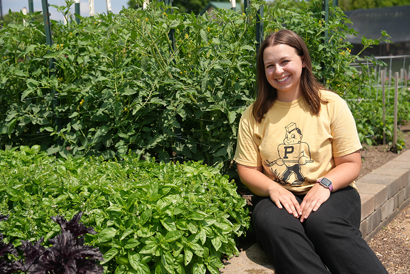 Kayla Grennes poses by basil and tomato plants like the ones she works with