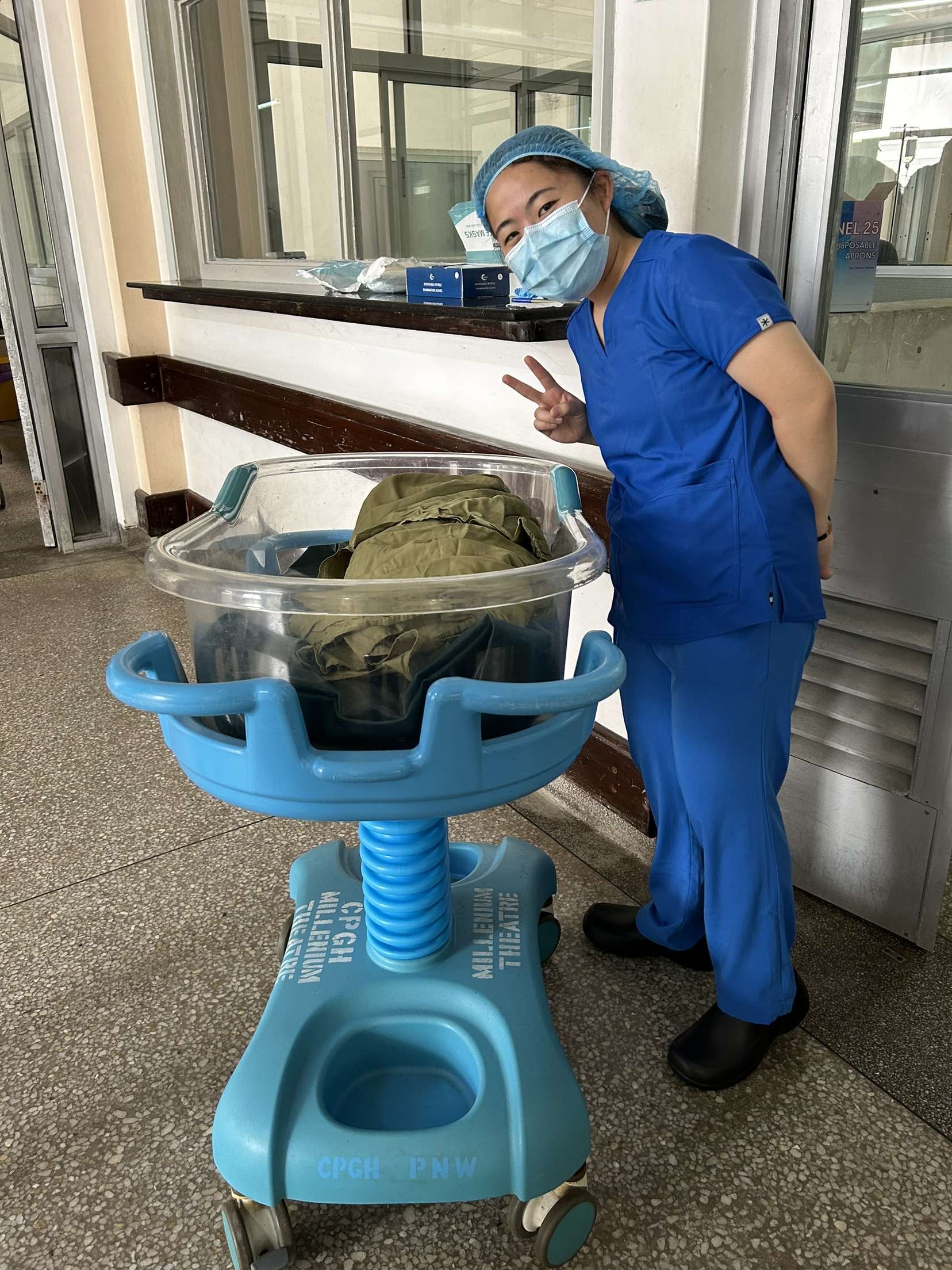 Jellings stands next to a plastic container for holding newborns in a hospital, wearing blue scrubs