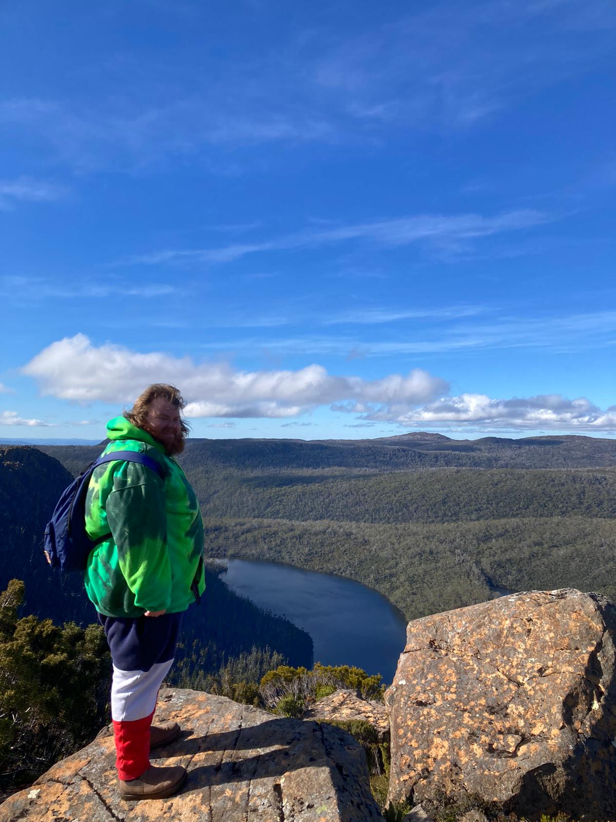 Cade Kane stands on a rocky cliff overlooking green hills