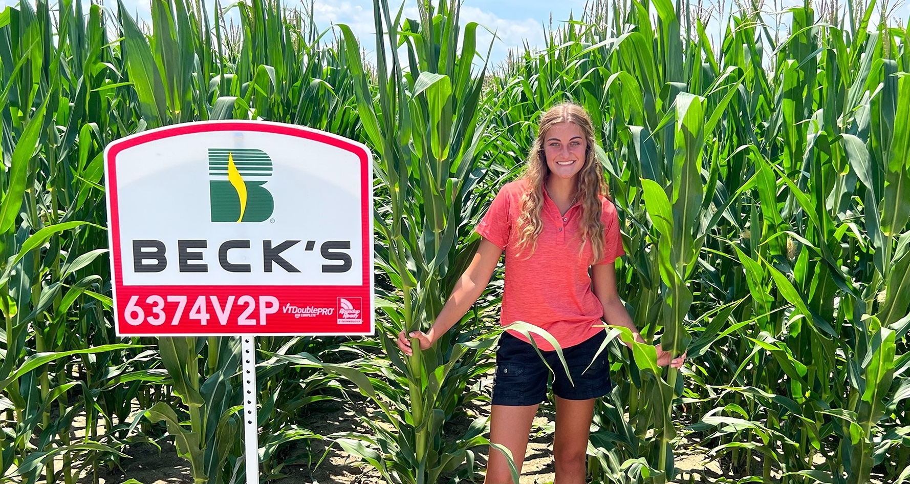 Mina Reising stands in corn field by Becky's Hybrid sign