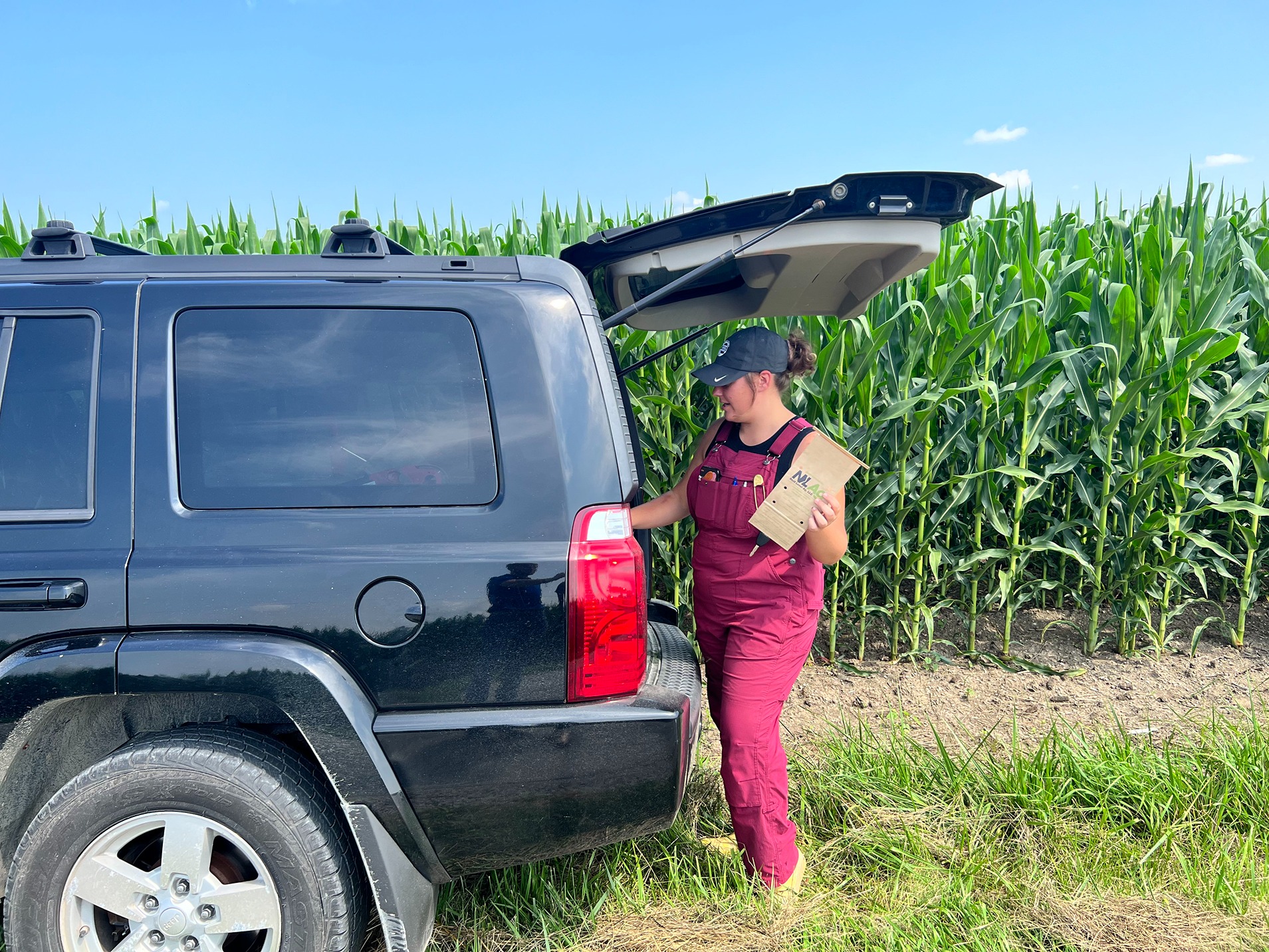 Madelyn Pierce gathers soil and tissue sampling supplies (a paper sample bag) from the trunk of her car to gauge the corn field's health