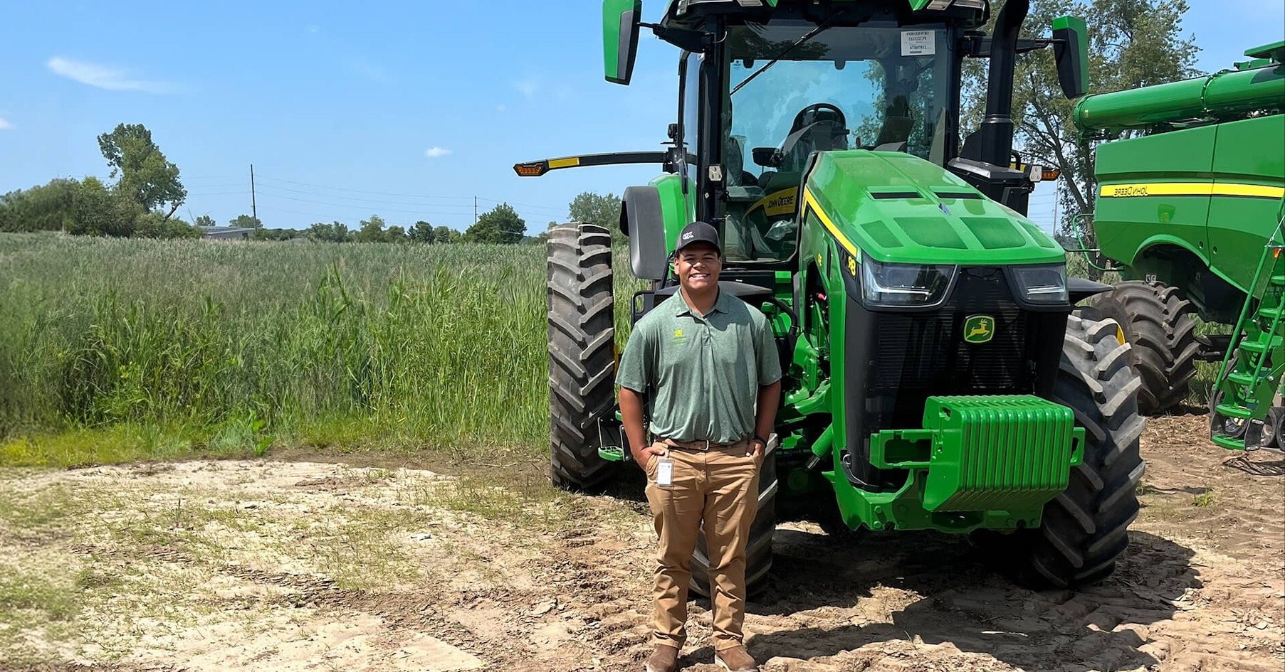 Drew Parker stands in front of a John Deere Tractor in a field.