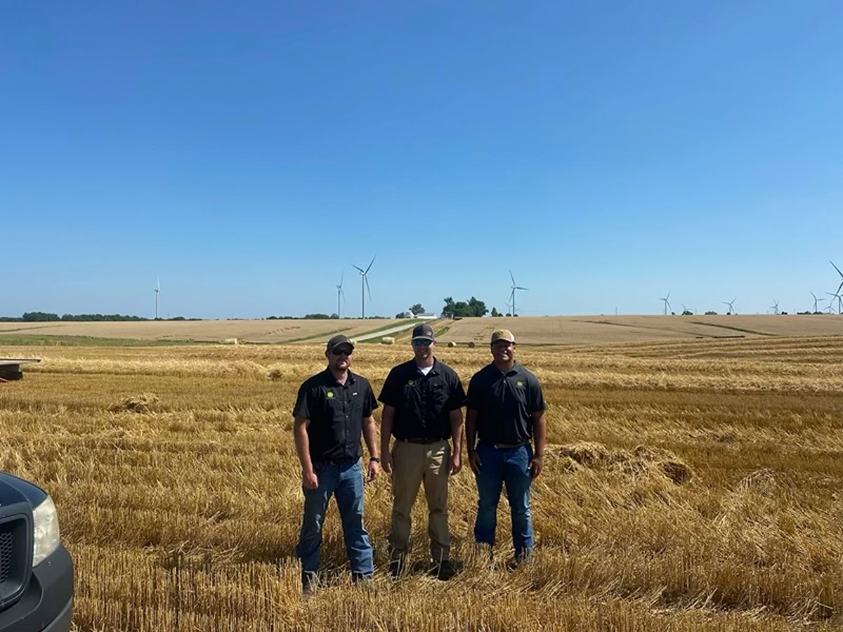 Drew Parker stands outside in a field with two of his mentors at John Deere. 