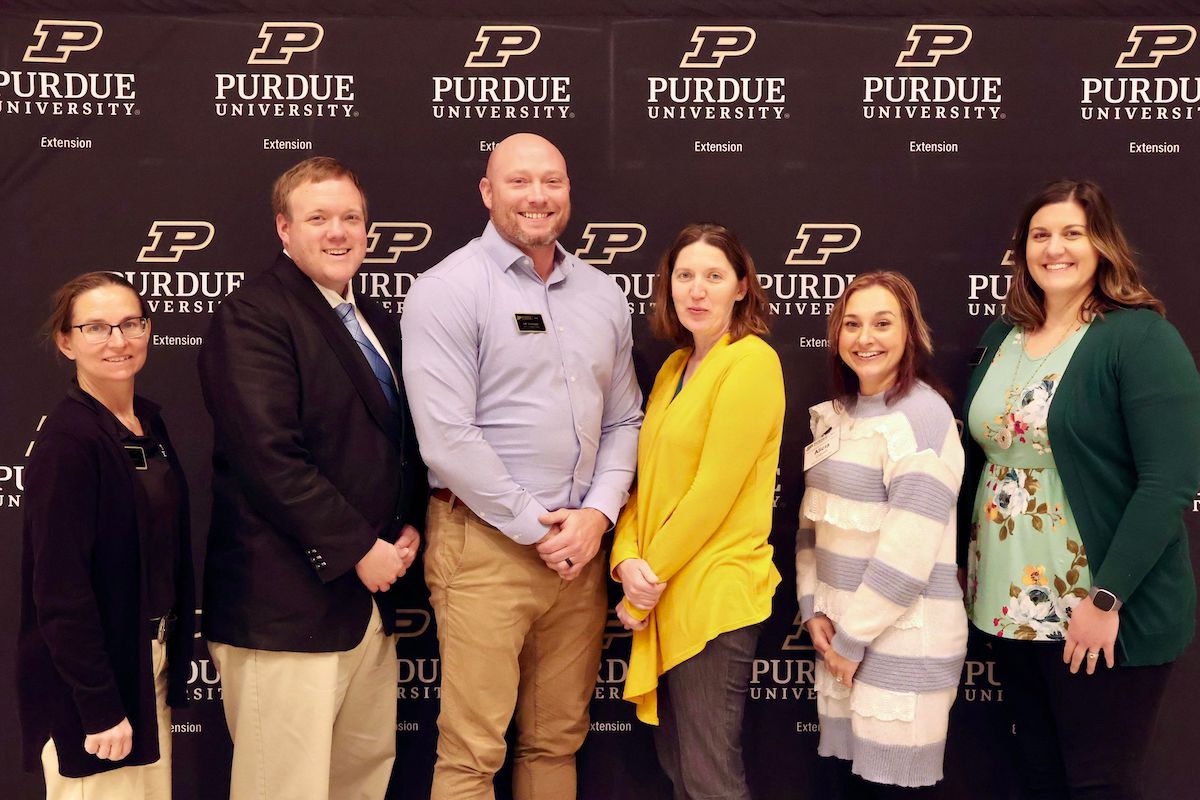 Purdue Extension faculty and educators smiling in front of Purdue banner in West Lafayette, Indiana