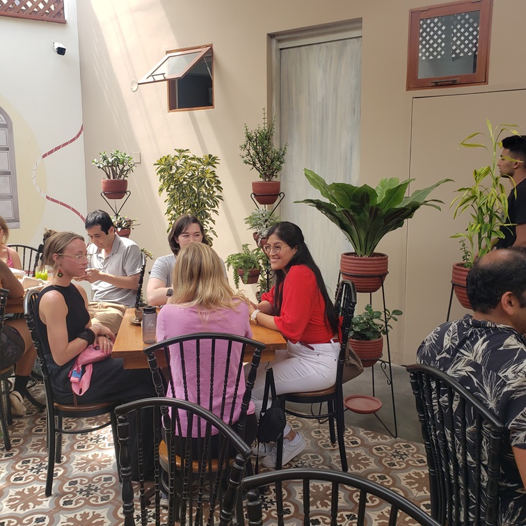 Students talking at tables with potted plants surrounding them