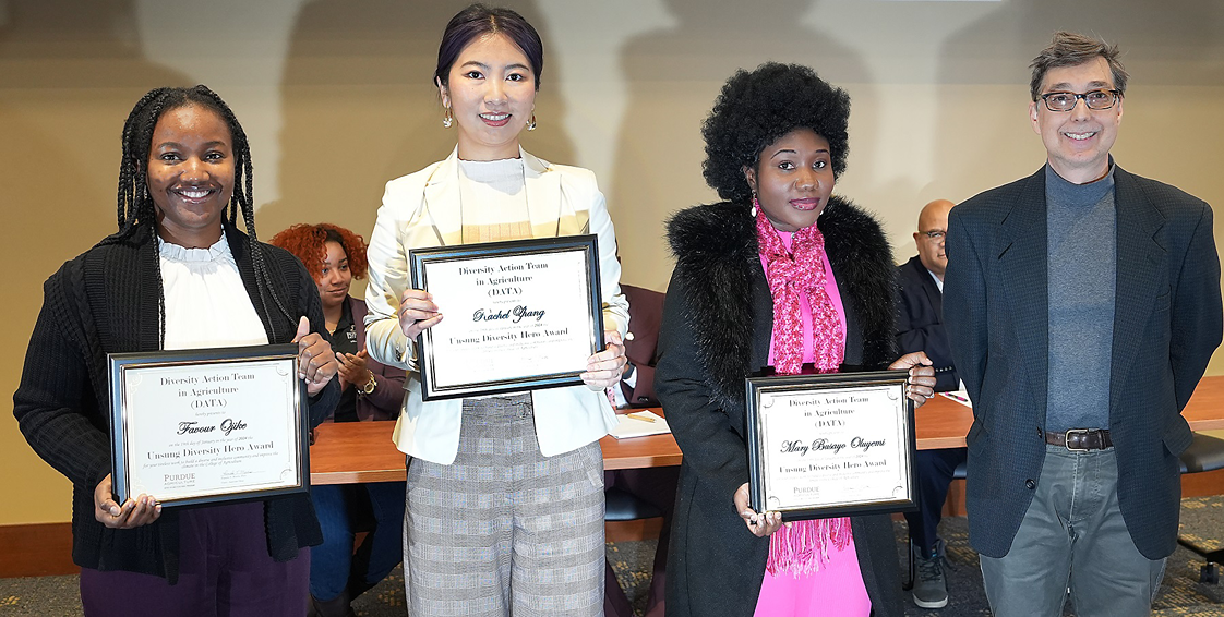 Three students pose with certificates and the award presenter stands at the right