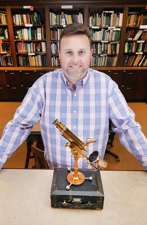 Simmons stands in the Purdue Herbaria with his antique brass microscope