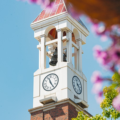Purdue's bell tower stands tall behind a foreground of purple petunias