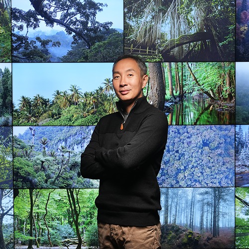 Jingjing Liang stands tall in front of a wall of monitors showing pictures of different forests.