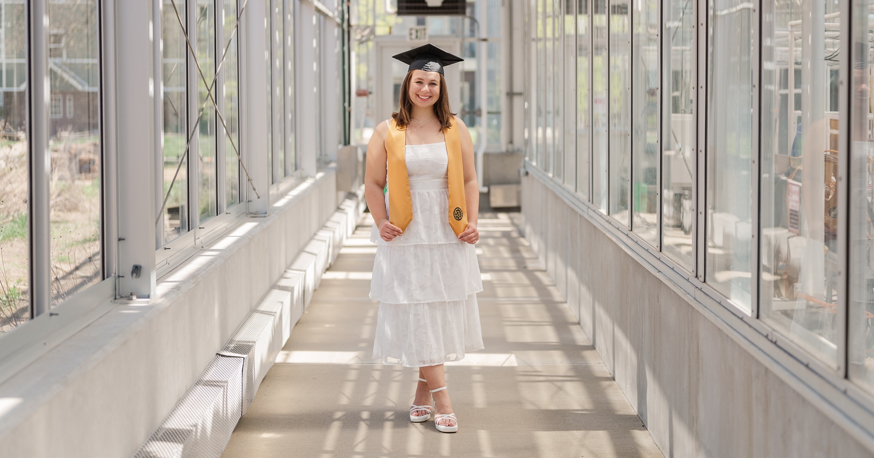 Senior Kayla Grennes stands in cap and sash in Purdue Greenhouse 
