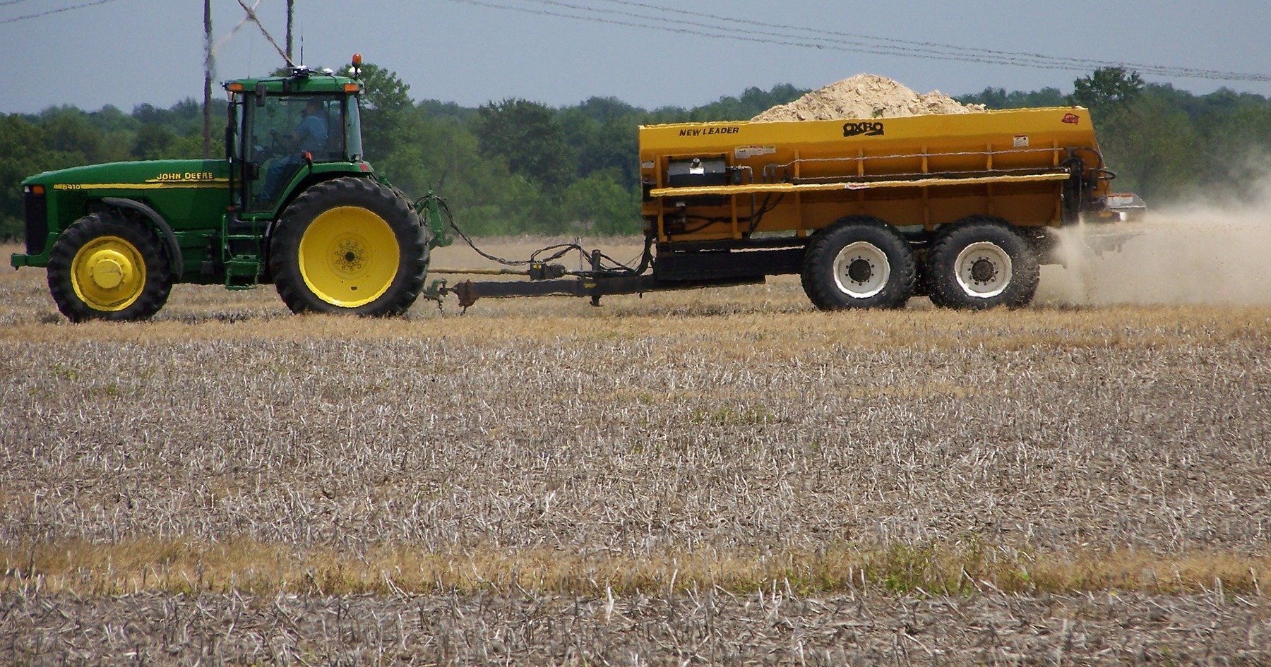a tractor spreads gypsum across a field and a soil probe has a sample of six inches of a dark brown soil in the metal tube
