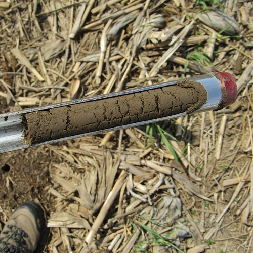 a tractor spreads gypsum across a field and a soil probe has a sample of six inches of a dark brown soil in the metal tube