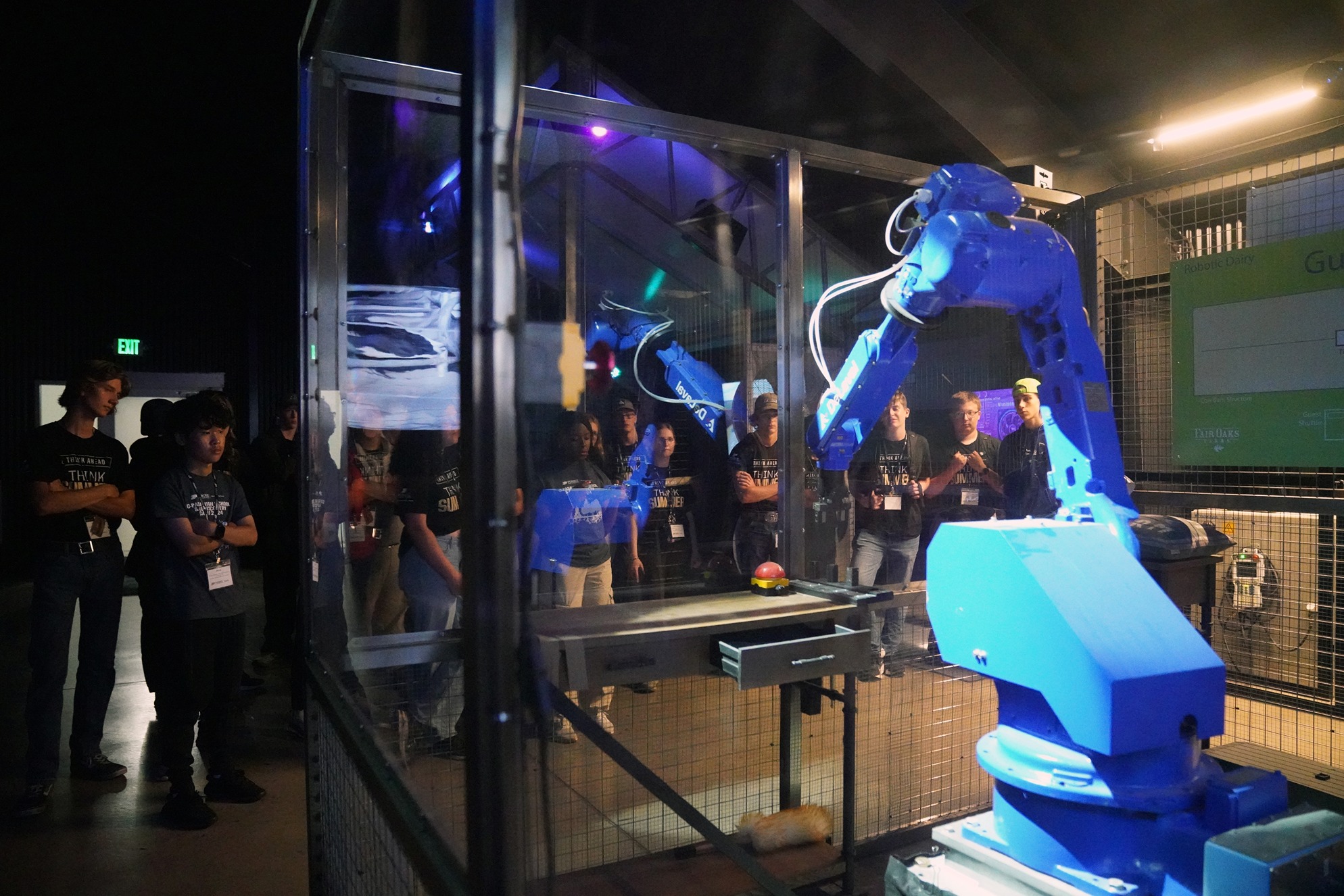 Students standing behind protective glass watching a robotic arm ring a bell