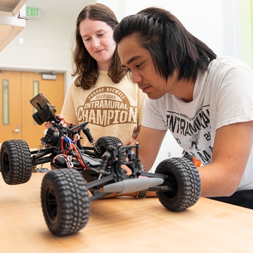 two students lean over a counter as the tinker on a remote controlled car together